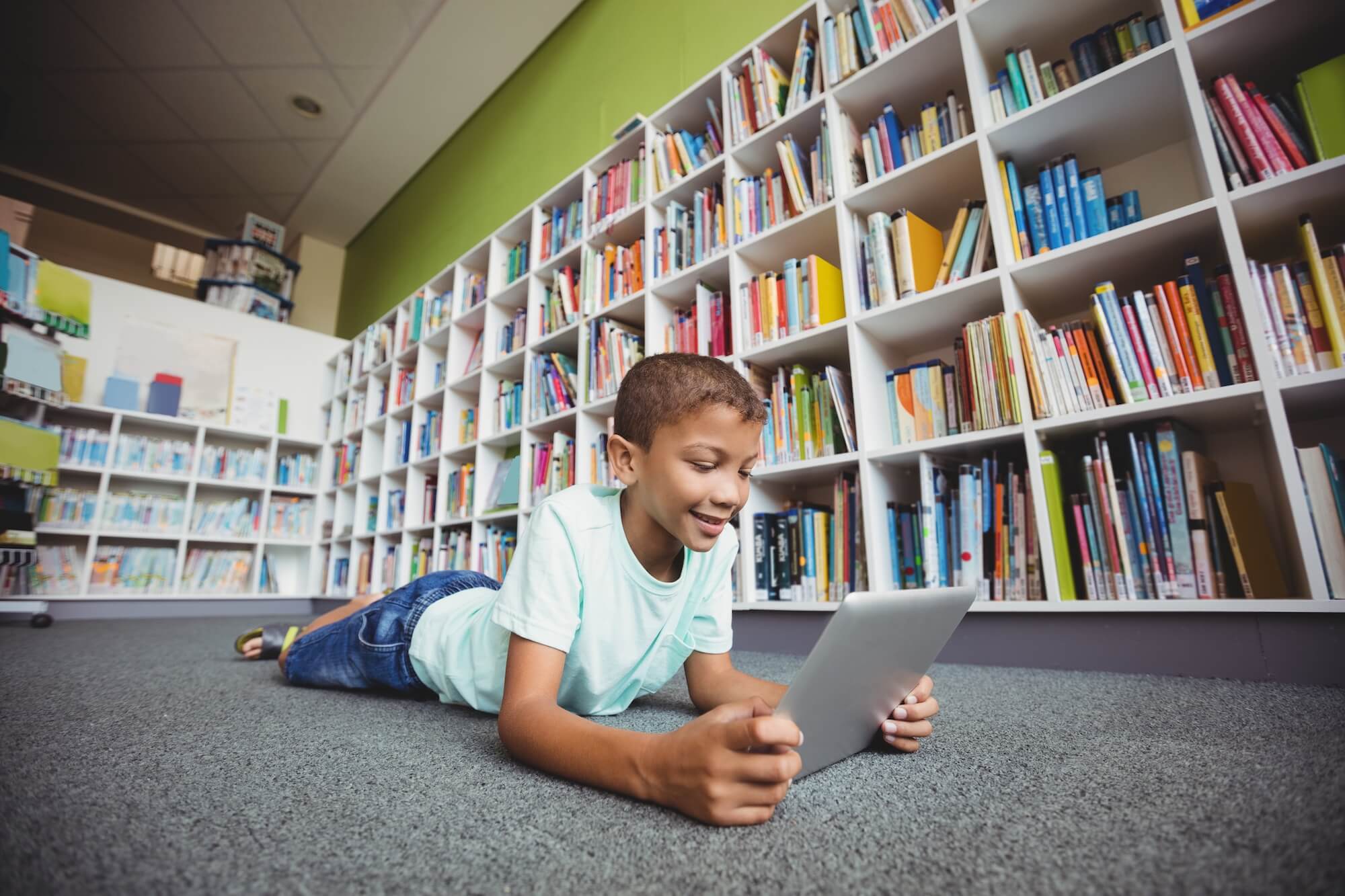 Student laying down looking at a tablet in a library